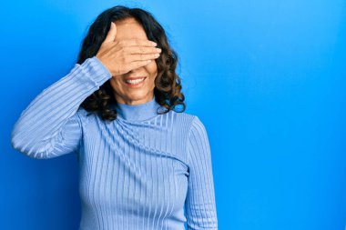 Orta yaşlı İspanyol kadın, sıradan kıyafetler giyiyor, gülümsüyor ve yüz yüze gülüyor. Şaşırtmak için gözleri örtüyor. kör kavram. 