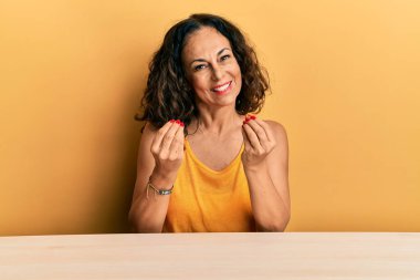 Güzel orta yaşlı kadın, gündelik giysiler içinde masada oturuyor, elleriyle para hareketi yapıyor, maaş istiyor, milyonerlik işi yapıyor. 