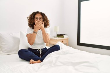 Orta yaşlı İspanyol bir kadın evde yatağında oturuyor ve yanlışlıkla elleriyle ağzını kapatıyor. gizli kavram. 