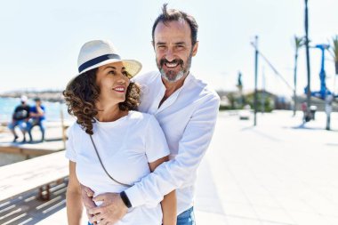 Orta yaşlı İspanyol çift, mutlu bir şekilde gülümsüyor ve gezinti alanında sarılıyorlar..