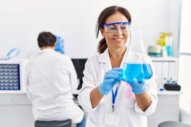 Laboratuvarda deney tüpü tutan bilim adamı üniforması giyen orta yaşlı erkek ve kadın partnerler.
