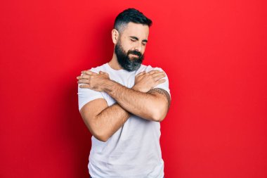 Gündelik beyaz tişört giyen genç İspanyol adam mutlu ve pozitif, kendinden emin bir şekilde kendine sarılıyor. Sevgi ve özgüven. 