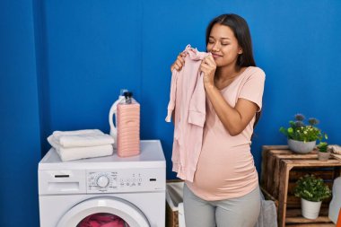 Çamaşırhanede temiz bebek kıyafetleri kokan genç Latin kadın hamile.