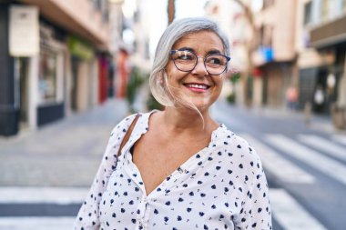 Orta yaşlı bir kadın sokakta kendine güvenerek gülümsüyor.