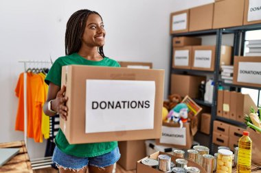 Gönüllü üniforma giyen genç Afrikalı Amerikalı kadın bağış paketini yardım merkezinde tutuyor.