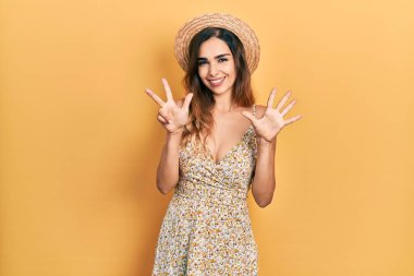 Genç İspanyol kız yaz şapkası takıyor ve 8 numaralı parmaklarıyla işaret ederken kendinden emin ve mutlu gülümsüyor.. 