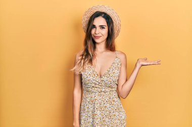 Yazlık şapkalı genç İspanyol kız neşeli bir şekilde sunum yapıyor ve avuç içiyle kameraya bakıyor.. 