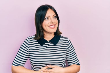 Gündelik kıyafetler giyen genç İspanyol kadın yüzünde gülümsemeyle yan yana bakıyor, doğal bir ifade. Kendinden emin gülen. 