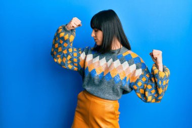 Sıradan bir kazak giyen genç İspanyol kadın gururla gülümseyen kol kaslarını gösteriyor. fitness konsepti. 