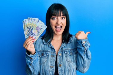 Genç İspanyol kadın elinde 100 Romen Ley banknotuyla baş parmağını kaldırmış, ağzı açık gülümsüyor. 