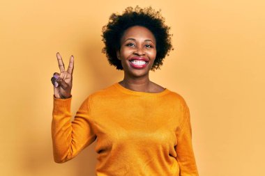 Gündelik giysiler giymiş genç Afro-Amerikan kadın kameraya bakıp zafer işareti yapıyor. İki numara.. 