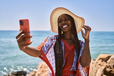 Gülümseyen Afrikalı Amerikalı genç bir kadın sahildeki akıllı telefondan selfie çekiyor..