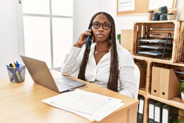 Ofiste çalışan örgülü zenci kadın telefonda konuşurken yüzünde ciddi bir ifadeyle rahatladı. Basit ve doğal bir şekilde kameraya bakıyorsun.. 