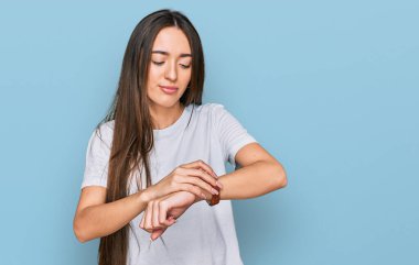Gündelik beyaz tişört giyen genç İspanyol kız kol saatini kontrol ediyor, rahat ve kendinden emin. 