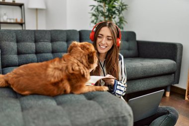 Genç İspanyol kadın dizüstü bilgisayar kullanıyor. Evde köpekle oturuyor.