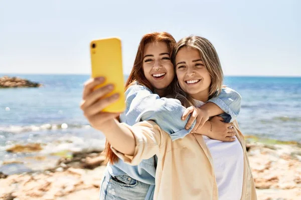 Kumsalda birbirine aşık iki genç lezbiyen kadın. Güzel kadınlar sahilde romantik bir ilişki içinde. Akıllı telefonla selfie çekiyorlar.