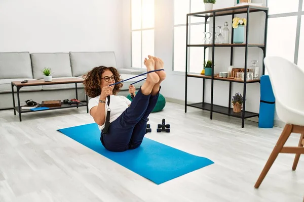 Olgun İspanyol kadın evdeki oturma odasında lastik bantlarla egzersiz yapıyor.