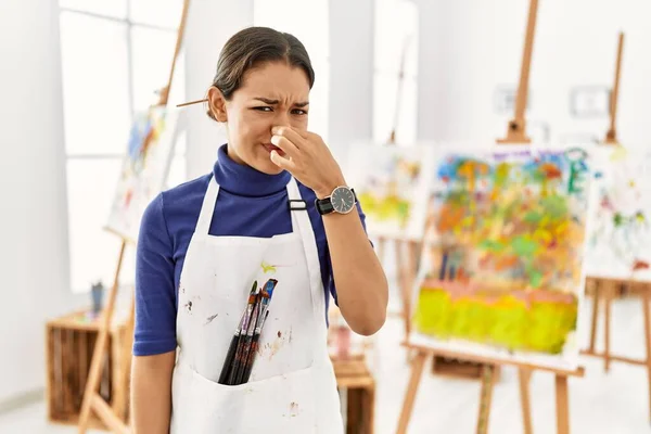艺术工作室里的年轻的黑发女人闻到一股难闻难闻的气味 用手指捂住鼻子屏住呼吸 — 图库照片