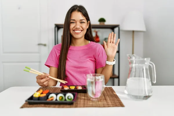 若いブルネットの女性が箸を使って寿司を食べることこんにちは幸せと笑顔 優しい歓迎ジェスチャー — ストック写真