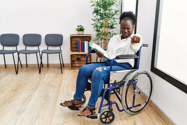 Bekleme odasında tekerlekli sandalyede oturan genç siyahi kadın kameraya kızgın ve sinirli bir şekilde seni işaret ediyor. 