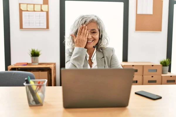 中年女商人坐在办公桌前 用手提电脑在办公室里用一只手捂住眼睛 脸上挂着自信的微笑 还有令人惊讶的情绪 — 图库照片