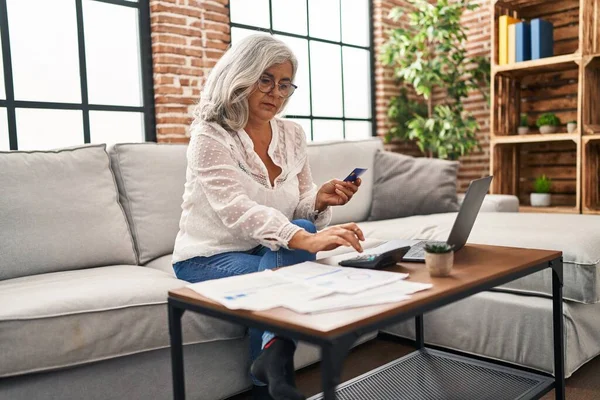 Evde dizüstü bilgisayar ve kredi kartı kullanan orta yaşlı kadın.