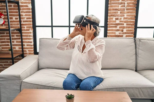 Evde sanal gerçeklik gözlüğü kullanan orta yaşlı bir kadın video oyunu oynuyor.