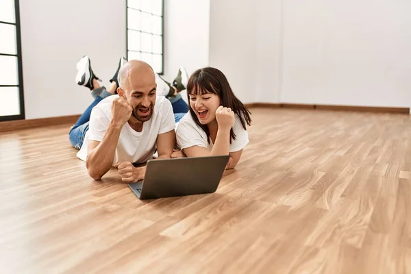 在空荡荡的新家使用笔记本电脑时 他的年轻夫妇笑得很开心 — 图库照片