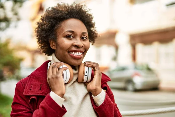 Afro saçlı, mutlu ve kendinden emin, kulaklık takıp müzik dinleyen güzel Afro-Amerikalı kadın.