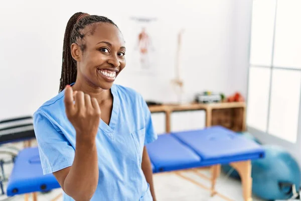 Black woman with braids working at pain recovery clinic beckoning come here gesture with hand inviting welcoming happy and smiling