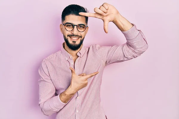 Sakallı, rahat gömlekli, gözlüklü, gülümseyen, elleri ve parmakları mutlu yüzlü yakışıklı bir adam. yaratıcılık ve fotoğrafçılık kavramı. 