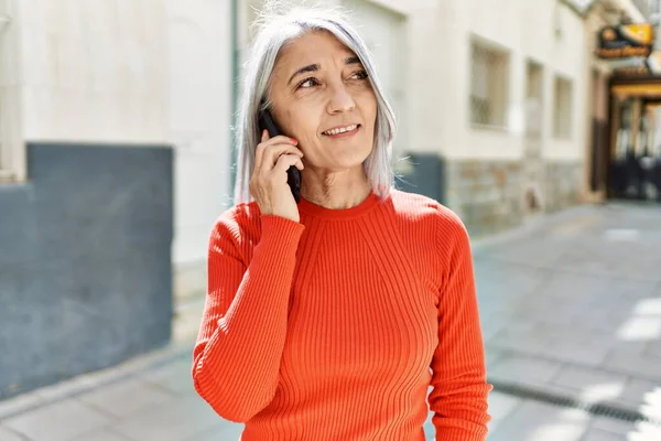 Orta yaşlı, kır saçlı, gülümseyen, mutlu, akıllı telefondan konuşan bir kadın..