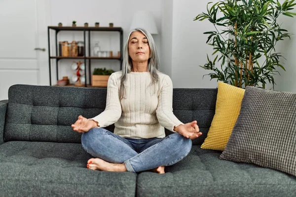 Orta yaşlı, kır saçlı kadın evde yoga egzersizi yapıyor.