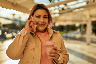 Genç İspanyol kız akıllı telefondan konuşuyor ve şehirde kahve içiyor..
