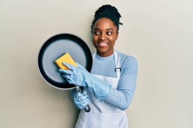 Saçları örülmüş, önlük takmış, elinde kırbaç tutan, gülümseyen ve kafasını çeviren Afro-Amerikalı bir kadın.. 