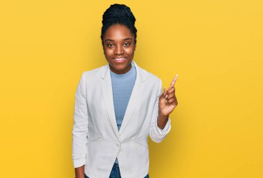 Genç Afro-Amerikalı kadın iş kıyafetleri giymiş, yüzünde kocaman bir gülümseme var, kameraya el ile işaret ediyor.. 