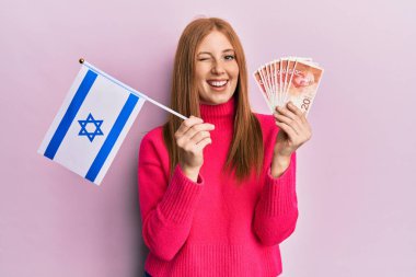Genç İrlandalı bir kadın elinde İsrail bayrağı ve şekel banknotları ile kameraya bakıyor. Seksi bir ifadeyle, neşeli ve mutlu bir yüzle.. 