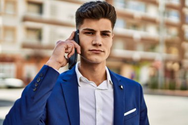 Akıllı telefondan konuşan genç adam sokakta takım elbise giyiyor.