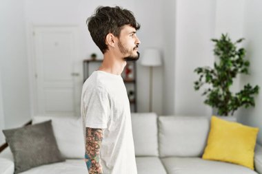 Oturma odasında sakallı İspanyol bir adam. Yan yan bakıyor, profil pozu veriyor. Doğal bir yüzü ve kendine güvenen bir gülümsemesi var.. 