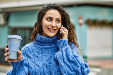 Genç İspanyol kadın akıllı telefondan konuşuyor ve şehirde kahve içiyor..