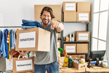 Gönüllü olarak bağış kutusunu tutan yakışıklı orta yaşlı adam seni ve kamerayı işaret ediyor, pozitif ve neşeli gülümsüyor. 