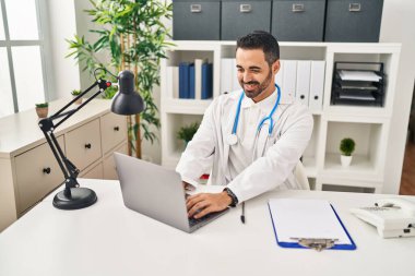 Klinikte çalışan dizüstü bilgisayar kullanan doktor üniforması giyen genç bir İspanyol.