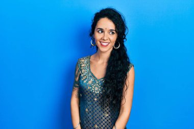 Bindi ve geleneksel kurta elbisesi giyen genç bir kadın yüzünde gülümsemeyle yan yana bakıyor, doğal bir ifade. Kendinden emin gülen. 