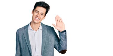 İş kıyafetleri giymiş genç İspanyol adam merhaba diyor mutlu ve gülümsüyor, dostça karşılama jesti. 