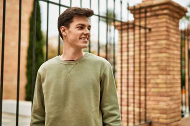 Genç İspanyol adam gülümseyerek şehirde mutlu mesut dikiliyor..