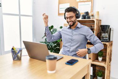 Genç Arap adam ofiste müzik dinlerken kendinden emin gülümsüyor.