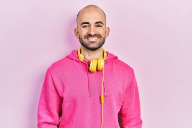 Spor kıyafetleri giyen, kulaklık takan, mutlu ve havalı gülümseyen genç kel bir adam. şanslı kişi. 