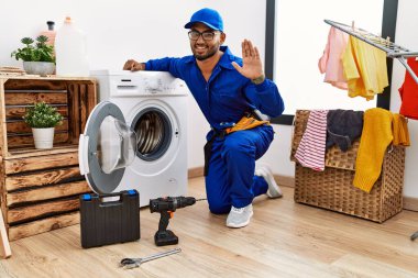 Çamaşır makinesinde çalışan genç Hintli teknisyen mutlu ve güler yüzlü bir şekilde selam veriyor. 