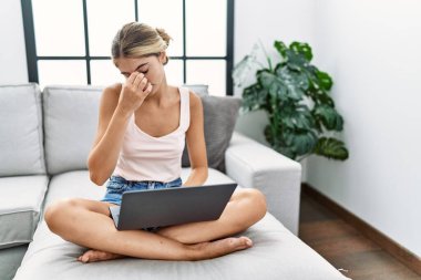 Genç sarışın kadın evinde dizüstü bilgisayar kullanıyor. Kanepede oturuyor. Burnunu ve gözlerini ovuşturup yorgunluk ve baş ağrısı çekiyor. Stres ve hüsran kavramı. 