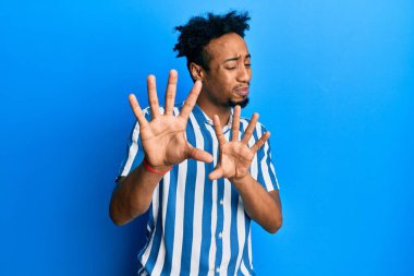 Sakallı, sıradan çizgili tişört giyen, tiksindirici ve tiksindirici bir ifade takınan, tiksinti tepkisi yüzünden tiksinti duyan genç Afro-Amerikan bir adam. Eller havada. 